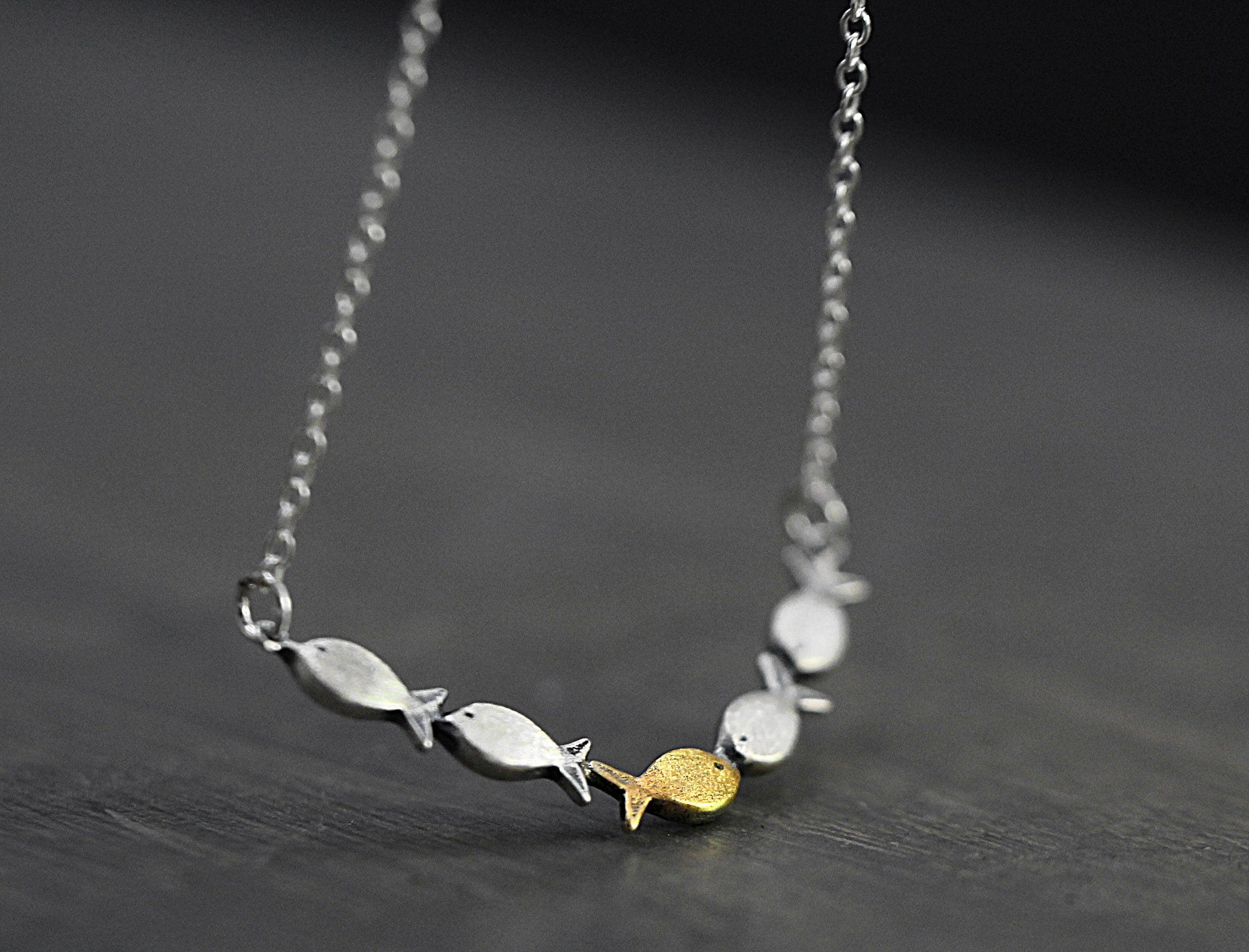 Swimming against the current. Dainty silver necklace. School of fish with one golden enameled fish swimming upstream. Gift for her.